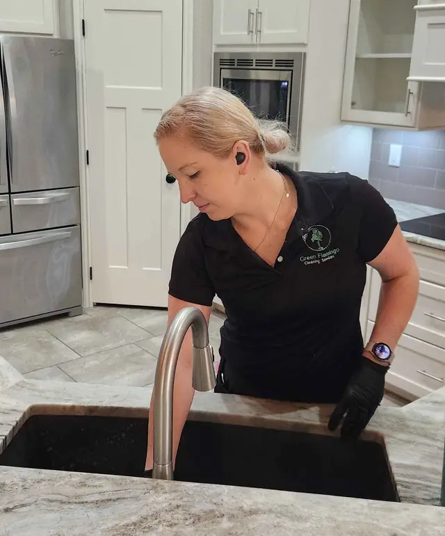 A Green Flamingo technician in black gloves scrubbing a stainless kitchen sink