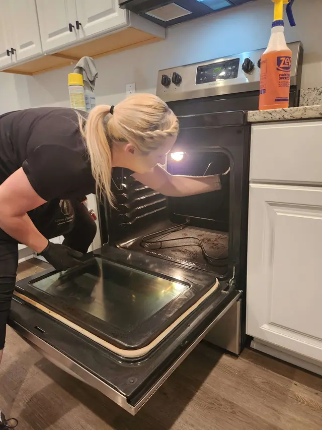 A technician in black gloves cleaning inside an open oven with a flashlight